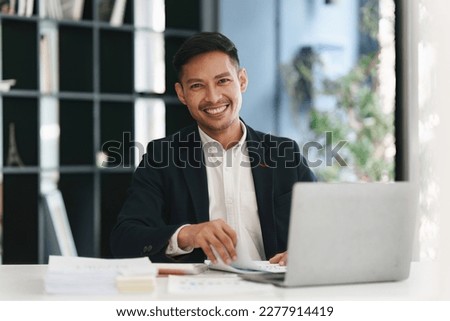 Smiling Asian Banker makes financial report and studies annual figures, analyzes profits. Accountant checks status of financial Royalty-Free Stock Photo #2277914419