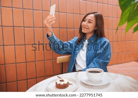 Portrait image of a young woman using mobile phone to take a selfie in cafe