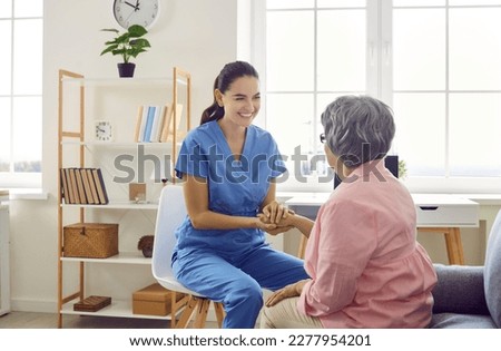 Happy friendly young caregiver or nurse in blue uniform scrubs smiling and holding a senior woman by the hand. Senior care, retirement home, medical help concept Royalty-Free Stock Photo #2277954201