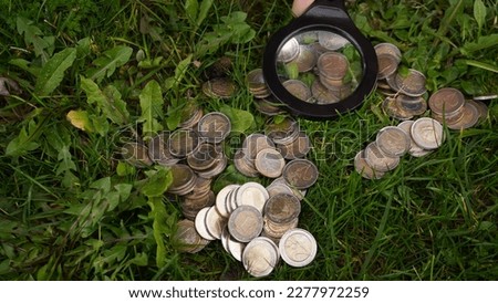         a child plays euro coins on the grass, looking at them through the preclusive glass                        