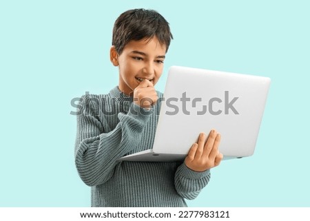 Little boy with laptop biting nails on blue background