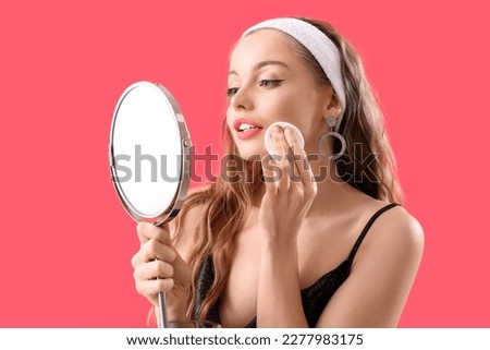 Young woman with mirror removing makeup on red background Royalty-Free Stock Photo #2277983175