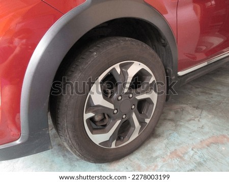 One of The Used and Worn Dirty Black Rubber Car Tire On The Light Blue Cement Garage Floor. Famous Branded Japanese Car. Red Car Paint. Beautiful Shot Close Up and Low Key Photography Image. JPG