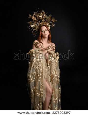 Close up fantasy portrait of beautiful woman model with red hair, goddess silk robes  ornate gold crown.  Posing with gestural hands reaching out, isolated on dark  studio background 