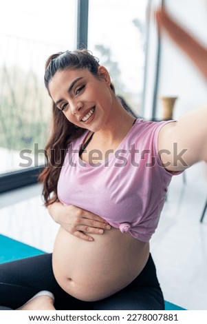 Beautiful pregnant young woman taking a picture of herself using her phone in a pink shirt