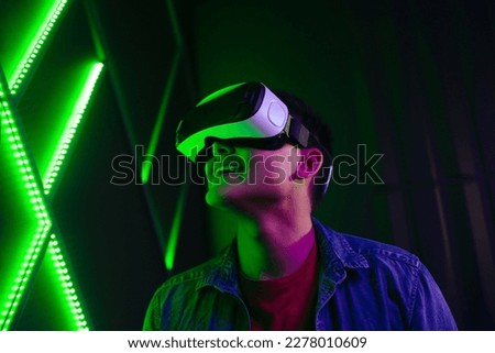 Man watching objects in virtual reality with a smile on his face. Tech-savvy young man experiencing an exciting game using VR goggles, immersing himself in the fun digital environment. Royalty-Free Stock Photo #2278010609