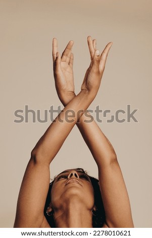 Young woman expressing herself with body movements, dancing gracefully with her arms raised. Woman with a lean body sculpture showcasing her flexibility and agility as she stands in a studio.