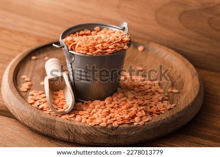 Red raw lentils in a metal bucket on a wooden background.