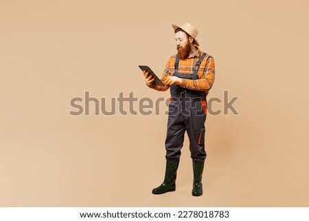 Full body young bearded man wears straw hat overalls gumboots work in garden hold clipboard with paper account documents isolated on plain pastel beige background studio portrait. Plant caring concept