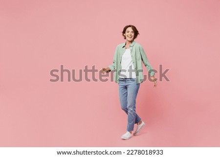 Full body young happy smiling cool cheerful woman 20s she wear green shirt white t-shirt look camera walking go isolated on plain pastel light pink background studio portrait. People lifestyle concept