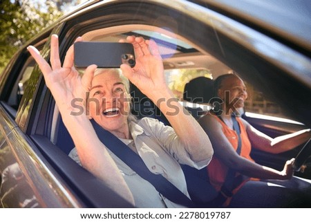 Passenger Taking Selfie On Mobile Phone As Two Senior Female Friends Enjoy Day Trip Out In Car