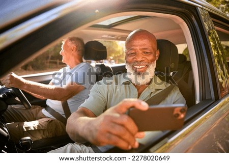 Passenger Taking Selfie On Mobile Phone As Two Senior Male Friends Enjoy Day Trip Out In Car