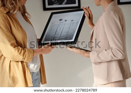 Close-up of two female restorers discussing black-and-white artwork in frame