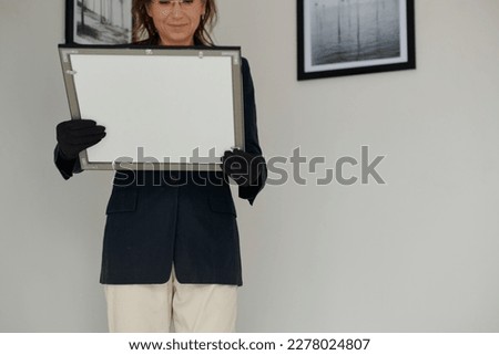 Female restorer in formalwear and black gloves holding picture in frame