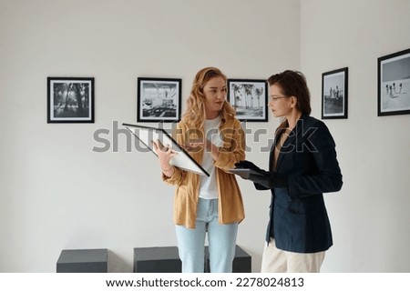 Two female workers of art gallery discussing restored picture