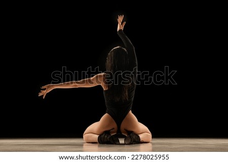 Back view. Young woman in bodysuit and heels dancing, performing, posing over black background. Concept of contemporary dance style, art, aesthetics, hobby, creative lifestyle, flexibility