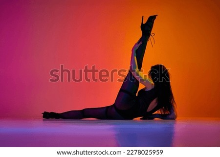 Stretching movements. Young woman dancing contemp over gradient pink orange studio background in neon light. Concept of contemporary dance style, art, aesthetics, hobby, creative lifestyle Royalty-Free Stock Photo #2278025959