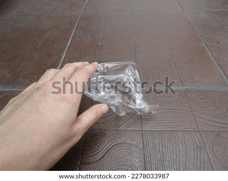 A Caring Hand Picks Up Transparent Plastic Food Wrap Trash From Above A Dark Brown Floor Photographed Close Up. Forms of A Resident's Concern for the Effects of Global Warming and Environmental Health