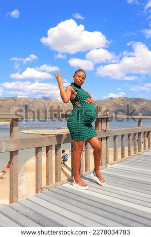 happy black pregnant woman standing on a wooden bridge the beach