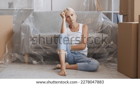 Sad relocation. Moving home. Eviction stress. Upset depressed tired pensive mature woman thinking of relocation in flat with boxes polyethylene covered furniture.