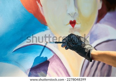 Girl artist hand holds paint brush and draws surreal fairy tale portrait on white canvas outdoor art painting festival, paintings art picture process. Woman artist paints atmospheric surreal picture