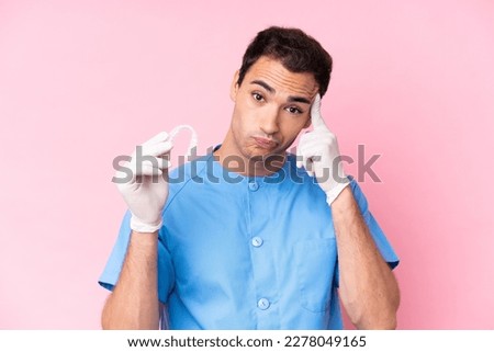 Dentist caucasian man holding invisible braces isolated on pink background thinking an idea