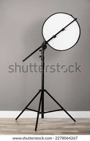 Professional light reflector on tripod near grey wall in room. Photography equipment