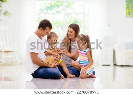Happy young family with kids at home. Father, mother, daughter and son playing on the floor in living room. Mom, dad, little boy and girl holding pet cat. Parents and children play together. Royalty-Free Stock Photo #2278078995