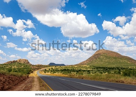 Hot day, lush clouds float in the blue sky. Paved highway crosses flat savannah. Travel to Africa. The magical desert in Namibia. 