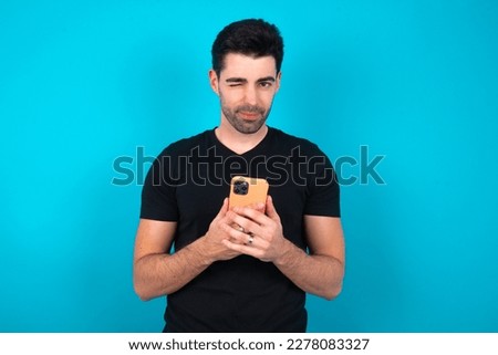 Young caucasian man wearing black T-shirt over blue background taking a selfie  celebrating success