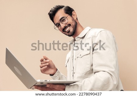 Portrait of a stylish man smile with teeth with a laptop in the hands of a freelancer, on a beige background in a white t-shirt, fashionable clothing style, space space