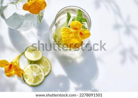 Iced lemonade with edible nasturtium flowers, lime and mint leaves. Refreshing summer drink. Healthy organic summer soda drink. Detox water. Diet unalcolic coctail. Royalty-Free Stock Photo #2278091501