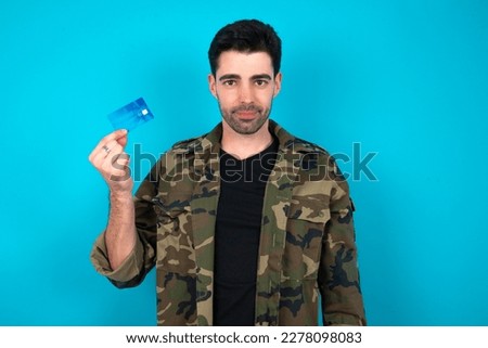 Photo of happy cheerful smiling positive Young man standing over blue studio background recommend credit card