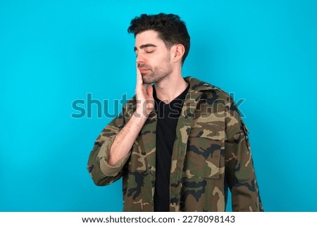 Young man standing over blue studio background with toothache