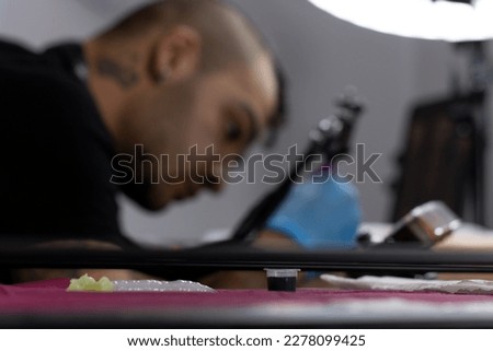 portrait of a young tattoo artist tattooing in the background with selective focus on the tattoo ink canister