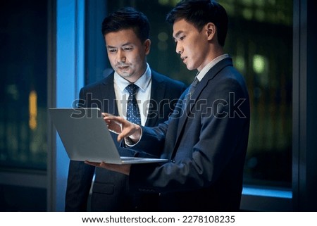 two asian corporate executives standing by the window in office discussing business using laptop computer at night Royalty-Free Stock Photo #2278108235