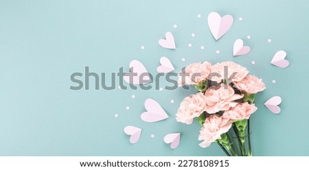 Pink carnation flowers and paper hearts on pastel blue background for Mothers day card.