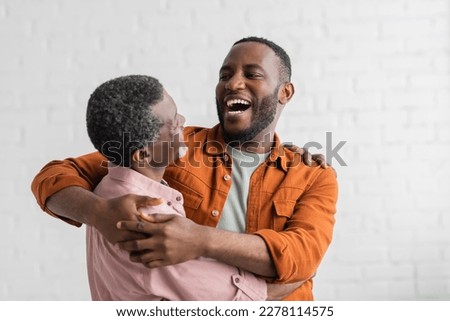 Positive african american son hugging mature father in living room Royalty-Free Stock Photo #2278114575