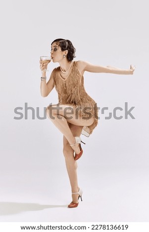 Wine party. Photo of gorgeous woman wearing chic old-time clothes holding cocktail glass and drinking over white background. Concept of beauty, art, vintage, retro style, rich party, american culture