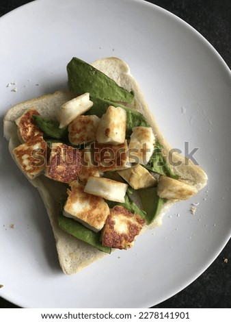 Slice of bread toast with fresh avocado and grilled halloumi cheese on white plate and plain black background vegetarian healthy breakfast lunch food photography closeup