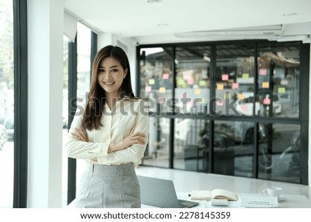 Happy young Asian saleswoman looking at camera welcoming client. Smiling woman executive manager, secretary offering professional business services holding digital tablet standing in office. Portrait Royalty-Free Stock Photo #2278145359