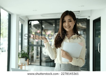 Happy young Asian saleswoman looking at camera welcoming client. Smiling woman executive manager, secretary offering professional business services holding digital tablet standing in office. Portrait Royalty-Free Stock Photo #2278145361