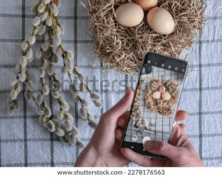 A girl takes pictures of Easter decorations on her smartphone. Nest with eggs and willow branches. Space for text. Easter concept