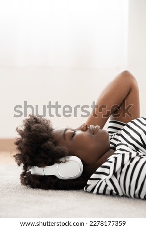 Black woman lying on floor and listening relaxing music on headphones