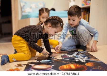 Children connecting jigsaw puzzle pieces in a kids room on floor at home.  Fun family activity leisure. 