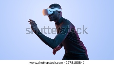 Side view of active young African American male athlete in black activewear running while exploring virtual reality in VR glasses against blue background