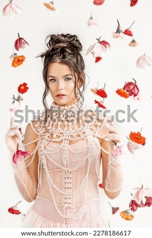 An attractive young woman in a pink short dress in a light spring studio with floating flowers. Beauty and fashion.