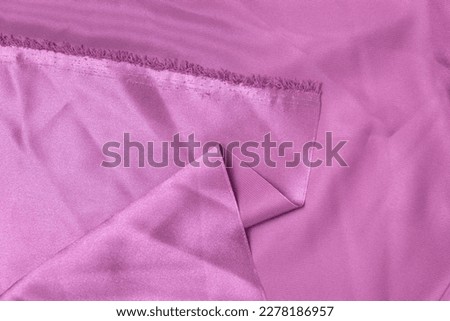 Folded pink-colored fabric texture background. This fabric is made of 100% polyester fibers.