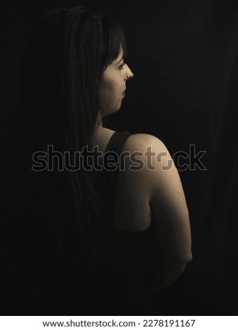 brunette girl is on her back with nose piercing looking to the side. black background. studio photography.