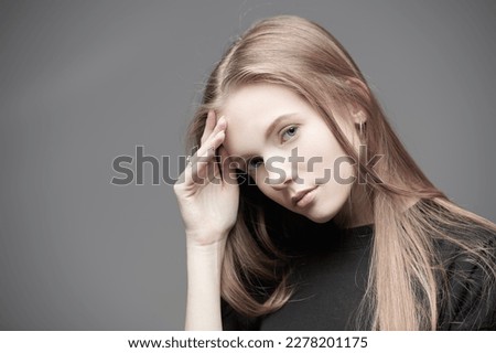 A beautiful tender girl with long red hair is sad about something. Dark gray studio background with copy space. Psychological art portrait. 